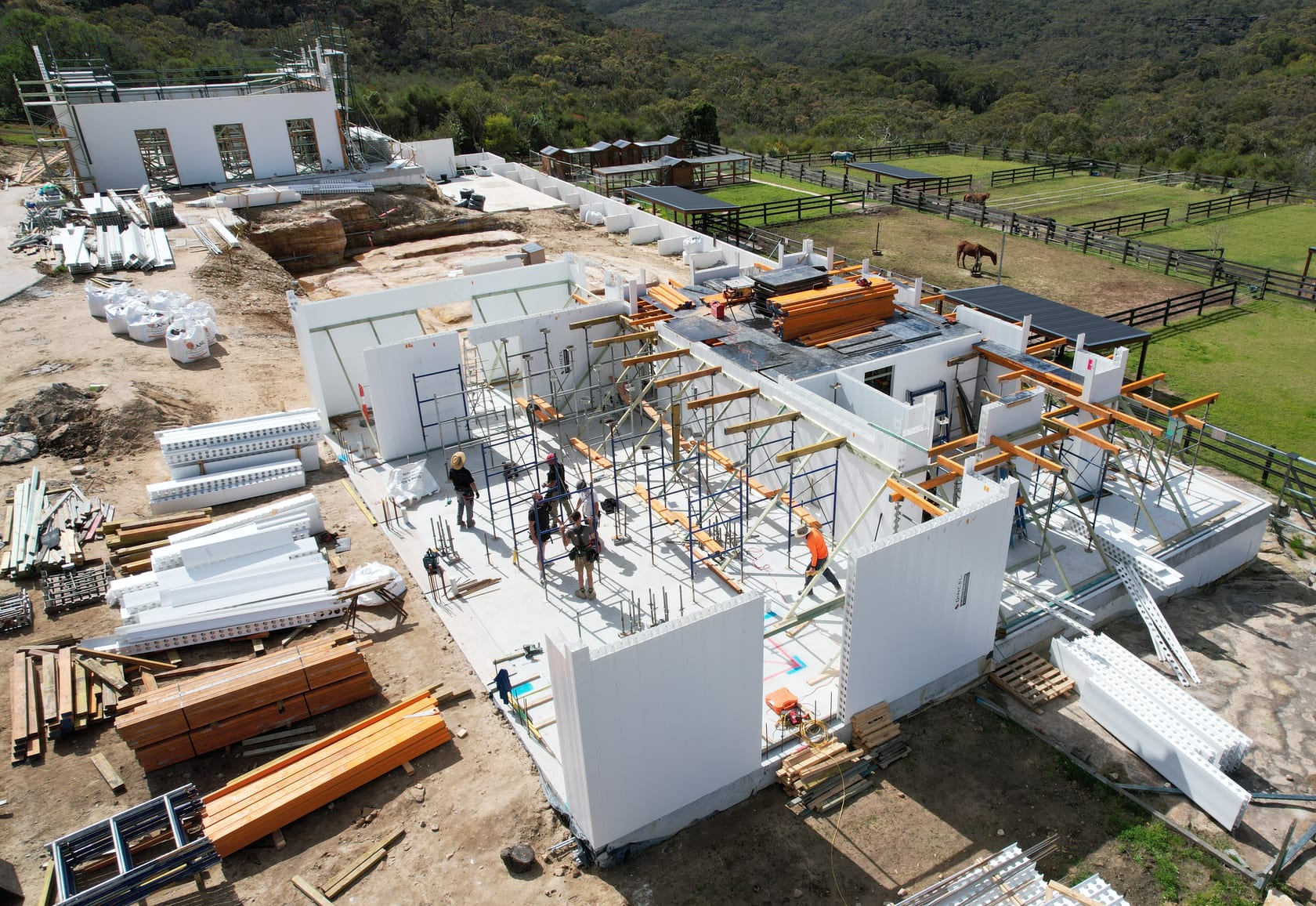 Aerial view of a large residential construction site with concrete slabs, wall panels, scaffolding and workers.